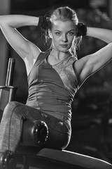 Woman doing strength exercises for abdominal muscles at indoor sport gym. Girl doing yoga stretches after running. Fitness model in dark sport club. Black and white.