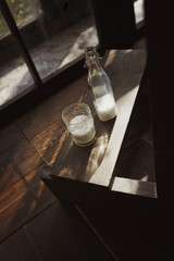 Beautiful clear glass and glass bottle filled with milk. Stand on a wooden surface. The vertical frame. Solar contrast light.