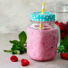 Mason jar mugs with fresh berry smoothies and fresh strawberries and raspberries on a gray stone or slate background. The concept of proper nutrition and health or detoxification.