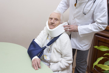 Lekarz ortopeda ze stetoskopem na szyi zakłada kołnierz ortopedyczny bardzo starej kobiecie...