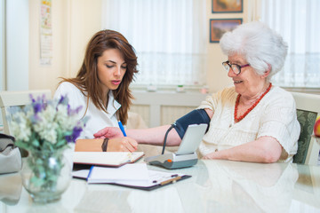 Young nurse measuring blood pressure of elderly woman at home.
