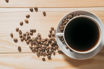 coffee is poured into a white cup with roasted coffee beans scattered on a wooden surface