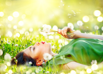 Naklejka premium Piękna młoda kobieta leży na polu w zielonej trawie i dmuchanie kwiatów mniszka lekarskiego. Koncepcja bez alergii