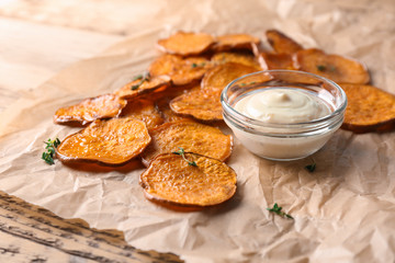 Parchment with tasty sweet potato chips and sauce on wooden table, closeup