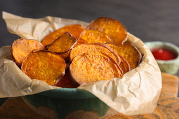 Bowl with tasty sweet potato chips on table, closeup