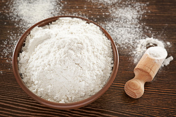 Bowl and scoop with wheat flour on wooden background