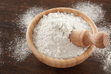 Bowl with wheat flour and scoop on wooden background