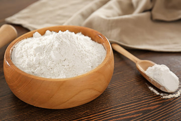 Bowl and scoop with wheat flour on wooden table