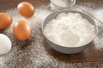 Fototapeta na wymiar Bowl with wheat flour and raw eggs on wooden table