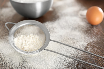 Sieve with wheat flour on wooden table