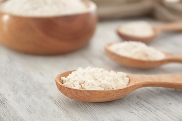 Spoon with wheat flour on wooden table, closeup