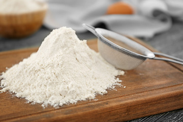 Heap of wheat flour and sieve on wooden board