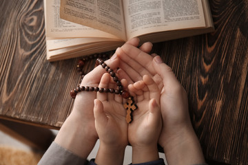 Religious Christian girl with her mother holding rosary beads at table, closeup