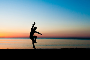 Fototapeta na wymiar Silhouette of man jumping in the air on the beach at sunrise.