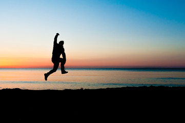 Silhouette of man jumping in the air on the beach at sunrise.