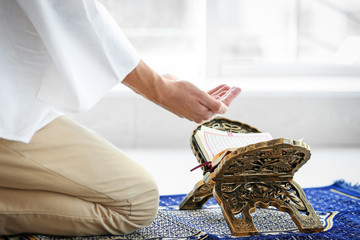 Young Muslim man praying over Koran on floor