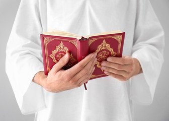 Young Muslim man reading Koran on light background