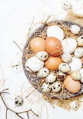 Fototapeta na wymiar Multicolored chicken and quail eggs with straw and branches, spring Easter composition, top view