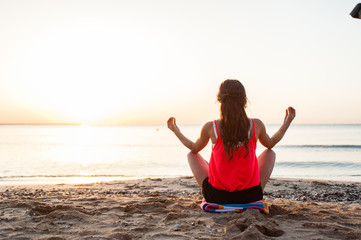 Silhouette young woman practicing yoga on the beach at sunrise.