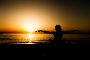Fototapeta premium Silhouette young woman practicing yoga on the beach at sunrise.