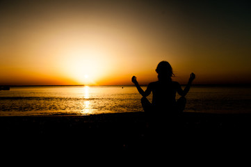 Silhouette young woman practicing yoga on the beach at sunrise.