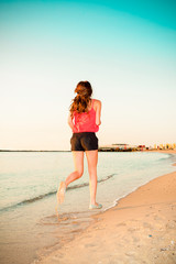 Woman running on beach during work out training. Fit beautiful young female model jogging at sunrise