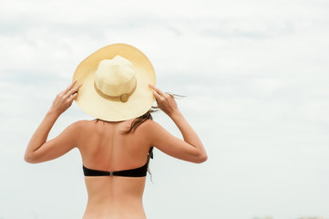 Fototapeta na wymiar Woman in straw hat on a tropical beach over sky