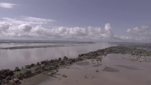 Aerial drone shot:  flying over floods affected houses with rising water along the river and drowning fields in a rural area. The main road still passable by cars and motorcycles