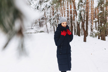 Fototapeta na wymiar The girl walks in a snow-covered forest among the pines in red gloves