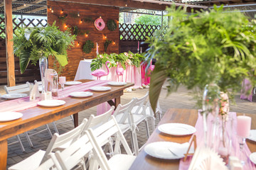Decoration for a wedding ceremony on a back yard with tables, plates, and vases full of anthurium flowers and monstera leafs. Pink and green colors. Space for text