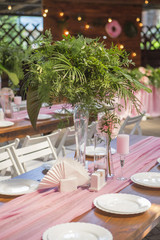 Decoration for a wedding ceremony on a back yard with tables, plates, and vases full of anthurium flowers and monstera leafs. Pink and green colors. Space for text