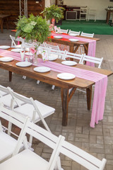 Decoration for a wedding ceremony on a back yard with tables, plates, and vases full of anthurium flowers and monstera leafs. Pink and green colors. Space for text