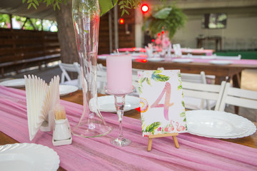 Decoration for a wedding ceremony on a back yard with tables, plates, and vases full of anthurium flowers and monstera leafs. Pink and green colors. Space for text