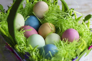 Colorful easter eggs in the decorative basket on a white wooden background