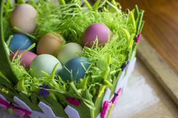 Colorful easter eggs in the decorative basket on a white wooden background