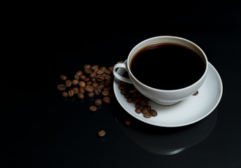 coffee is poured into a white cup with roasted coffee beans scattered on a black surface table