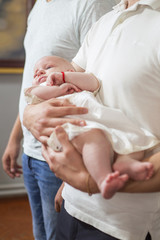 Godfather (caucasian young man) holding little infant kid in baptism (christening) ceremony in church