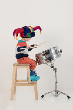 Happy Caucasian child drummer in a carnivalous fool's cap plays on a new drum set. Parents bought the boy a drum for training. Kid in bright clothes with new sticks in his hands be happy at home