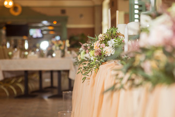 Wedding table decor full of rose and eustoma flowers, candles and peach colored fabric. Luxury rich restaurant interior. Indoor. Copy space