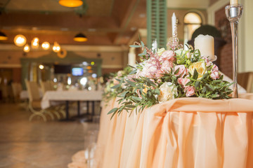 Wedding table decor full of rose and eustoma flowers, candles and peach colored fabric. Luxury rich restaurant interior. Indoor. Copy space
