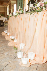 Wedding table decor full of rose and eustoma flowers, candles and peach colored fabric. Luxury rich restaurant interior. Indoor. Copy space