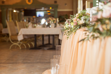 Wedding table decor full of rose and eustoma flowers, candles and peach colored fabric. Luxury rich restaurant interior. Indoor. Copy space