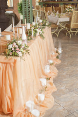 Wedding table decor full of rose and eustoma flowers, candles and peach colored fabric. Luxury rich restaurant interior. Indoor. Copy space