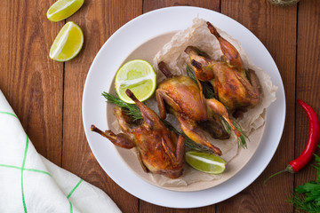 Appetizing baked quail with spices, herbs and lemon, lime in white dish on a wooden table Flat lay