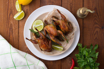 Appetizing baked quail with spices, herbs and lemon, lime in white dish on a wooden table