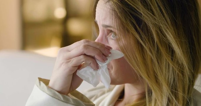 A woman sitting on the sofa in her house, cries desperately hugging the pillow and using the handkerchiefs to wipe away the tears. Concept of: despair, broken love, drama.