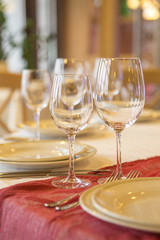 Set of glassess and plates on a wedding table surrounded by light garland and wine color flowers and tablecloth. Interior. Copy space