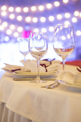 Set of glassess and plates on a wedding table surrounded by light garland and wine color flowers and tablecloth. Interior. Copy space