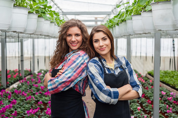 Pretty florists women working with flowers in a greenhouse with arms crossed, smiling.