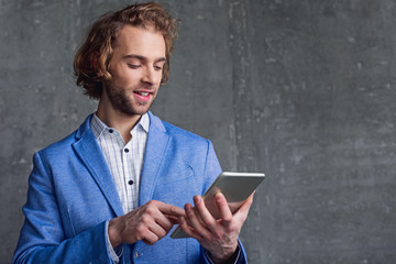 Portrait of cheerful bearded male using electronic tablet while keeping it in arm. Technology and career concept. Copy space